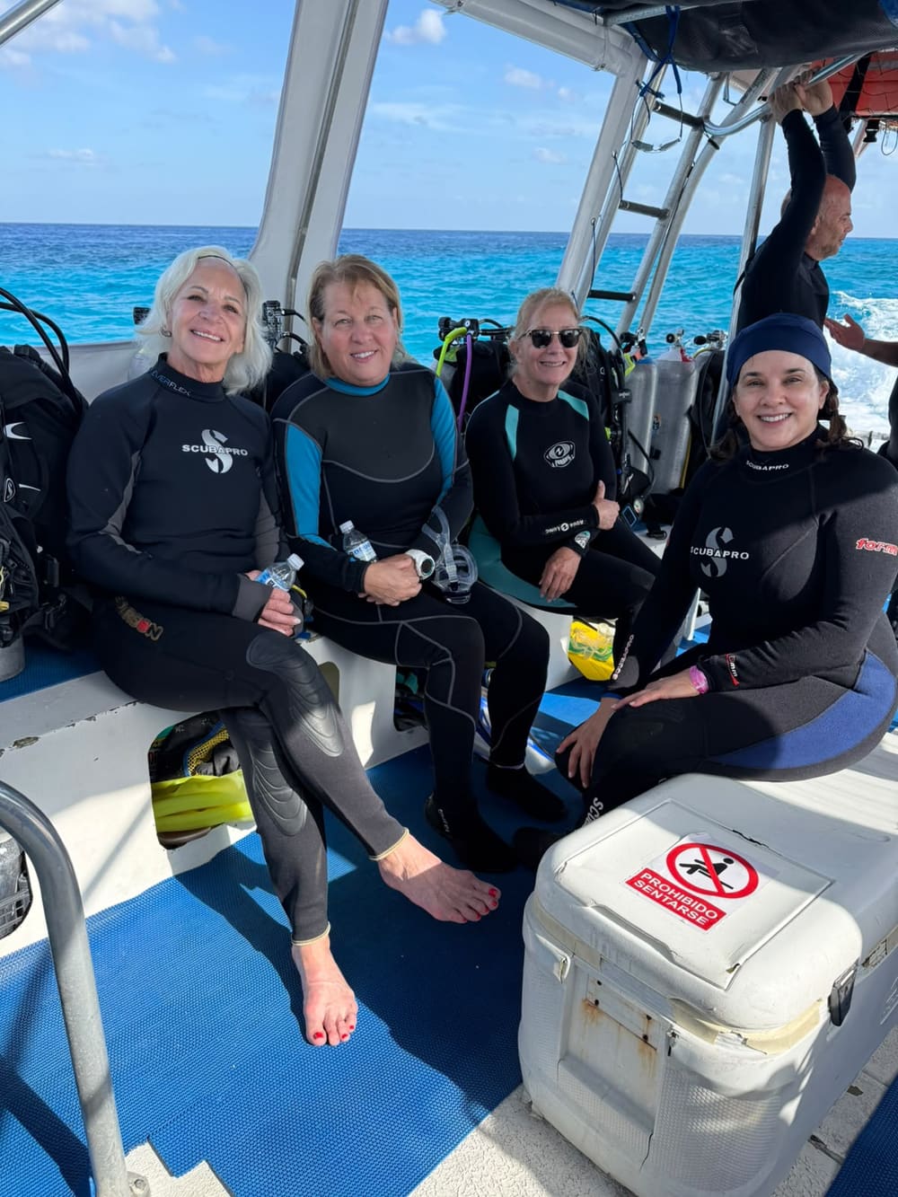Four divers in wetsuits on the boat, open blue water behind